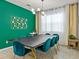 Elegant dining room with a modern table, teal velvet chairs, an emerald accent wall and stylish lighting fixture at 1999 Tropical Palms Cir, Kissimmee, FL 34747