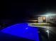 The pool glistens in the dark with blue lighting, adjacent to the house, creating a serene backyard retreat at night at 804 Starke Lake Cir, Ocoee, FL 34761
