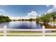 Scenic pond view with a white fence, trees, and clear blue sky with fluffy clouds at 2506 Shelby Cir, Kissimmee, FL 34743