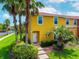 Charming yellow townhome featuring a red tile roof, lush landscaping, and a welcoming front entrance at 3002 Secret Lake Dr, Kissimmee, FL 34747