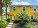 Bright yellow townhome featuring lush tropical landscaping and red tile roof, offering charming curb appeal at 3002 Secret Lake Dr, Kissimmee, FL 34747