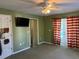 Green bedroom with a ceiling fan, TV, and striped curtains on patio doors at 11314 Huggins St, Leesburg, FL 34788