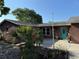 Charming brown home featuring a turquoise door and lush landscaping with vibrant plants and a red hibiscus at 11314 Huggins St, Leesburg, FL 34788