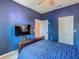 This bedroom has deep blue walls, a mounted television and an inviting queen sized bed with a patterned blue comforter at 2860 Orange Haven Way, Kissimmee, FL 34746