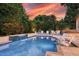 A beautiful backyard pool with a tranquil waterfall, lounge chairs, and lush landscaping against a colorful sunset backdrop at 1420 Palmer Ave, Winter Park, FL 32789