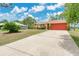 A large concrete driveway leads to a tan home with red garage doors, contrasting well with the clear blue sky at 2772 Pelham Cir, Deltona, FL 32738