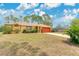 A tan, one-story home features a red garage door and landscaping. Grass yard shows evidence of drought at 2772 Pelham Cir, Deltona, FL 32738