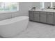 Bright bathroom featuring a sleek, free-standing tub, marble floors, and gray cabinets at 8080 Peaceful Cir, Sanford, FL 32771