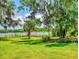 Lush backyard with sprawling green lawn, mature trees draped with Spanish moss, and a tranquil lake view at 3443 S Mellonville Ave, Sanford, FL 32773