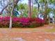 Charming home exterior with lush azalea bushes, mature trees, and a stone chimney, creating a serene, inviting landscape at 3443 S Mellonville Ave, Sanford, FL 32773