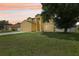 Two-story home with yellow stucco, attached garage, manicured lawn and mature trees at sunset at 670 Bluebill Ct, Poinciana, FL 34759