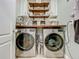 Bright and tidy laundry room features stainless steel appliances, wood shelves, and shiplap accents at 3980 Gadwall Pl, Leesburg, FL 34748