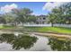 Backyard view showcases a serene pond, framed by mature trees, a white fence, and the home's exterior at 1803 Meadow Pond Way, Orlando, FL 32824