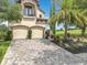 View of a stately two-story house with a balcony, two-car garage, brick driveway and tropical landscaping at 16246 Ravenna Ct, Montverde, FL 34756