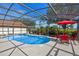 Screened-in pool featuring a bright red patio set, lush landscaping, a heated spa, and clear blue water at 404 Obo Dr, Davenport, FL 33896