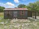 Backyard storage shed with red trim and open lean-to is surrounded by grass and some sparse vegetation at 8812 Oakwood Dr, Lake Wales, FL 33898