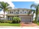 Two-story home with a gray exterior, manicured landscaping, palm trees, and a brick driveway leading to an attached garage at 2431 Tudor Rose Dr, Sanford, FL 32773