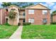 Exterior shot of townhome featuring brick facade, green lawn, sidewalk, trimmed bushes, and an upstairs balcony at 5545 Devonbriar Way # 206, Orlando, FL 32822