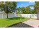 A well manicured backyard with green grass, a white fence, mature landscaping, and a paved patio at 8920 Palisades Beach Ave, Orlando, FL 32829