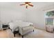 Bright bedroom with a ceiling fan, light wood floors, a large window, and a cozy bench at the foot of the bed at 8920 Palisades Beach Ave, Orlando, FL 32829