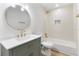 This bathroom has a sleek vanity with gold fixtures, a round mirror, and tiled shower and bath at 7440 Houston E Ct, Winter Park, FL 32792