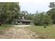Ranch-style home featuring a long covered front porch, gravel driveway, mature trees, and natural landscaping at 26586 Se Highway 42, Umatilla, FL 32784