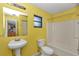Yellow bathroom with pedestal sink, toilet, tub, and a view to the kitchen at 6421 Nw 61St St, Ocala, FL 34482