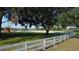 A spacious backyard with mature trees, lush green grass, a white fence, and a colorful playset, perfect for outdoor activities at 10809 Arrowtree Blvd, Clermont, FL 34715