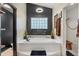 Soaking tub framed by tile and a unique glass block window plus a modern chandelier and black accent wall at 9774 Bohart Ct, Orlando, FL 32836