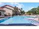 Community pool with shallow end, blue lounge chairs, a building, landscaping, and a clear blue sky at 3028 Parkway Blvd # 308, Kissimmee, FL 34747