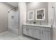 Bright bathroom featuring double sinks, white cabinetry, lighted mirrors, and tiled shower and floors at 9670 Cypress Pine St, Orlando, FL 32827