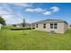 Landscaped backyard features green grass, a small tree, and the rear of a modern beige home with a gray roof at 928 Pearlwood Loop, Eagle Lake, FL 33839