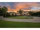 Stunning Mediterranean-style home with circular driveway, lush lawn and professional landscaping against a backdrop of a dramatic sunset at 11103 Bridge House Rd, Windermere, FL 34786