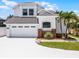Two story home featuring an attached two car garage, neutral paint, decorative brick detail, and tropical landscaping at 14423 Tambourine Dr, Orlando, FL 32837