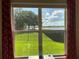 Picturesque window view of a lush green lawn and serene lake, framed by vibrant red curtains at 2258 Rickover Pl, Winter Garden, FL 34787