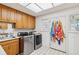 Bright laundry room featuring a tile floor, stainless steel washer and dryer, wood cabinets, and a sunny window at 3215 Greens Ave, Orlando, FL 32804