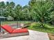 Relaxing backyard featuring a red chaise lounge on a travertine patio next to the grassy lawn and mature trees at 4454 Aspenwood Ct, Orlando, FL 32835
