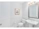 Clean powder room featuring white wainscoting, pedestal sink, toilet, and decorative mirror at 8480 Adalina Pl, Orlando, FL 32827