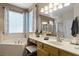 Bright bathroom with a soaking tub under a window with patterned curtains and a wooden vanity with a lighted mirror at 5063 Carillon Ln, Windermere, FL 34786