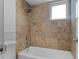 Tiled bathroom featuring a shower-over-tub combination and a natural stone tile surround with a window at 740 Florida Blvd, Altamonte Springs, FL 32701