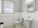 All-white bathroom with pedestal sink, toilet, and mirror above a window at 835 Antonette Ave, Winter Park, FL 32789