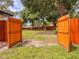 Open wooden gate provides access to the expansive, partially fenced backyard with mature trees at 8404 Singapore Ct, Orlando, FL 32817
