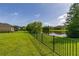 A serene backyard view with a lush lawn, black fence, and a tranquil pond surrounded by trees at 1113 Fieldstone Cir, Oviedo, FL 32765