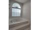 Elegant bathroom featuring a tiled-surround tub, and a large arched window with light-filtering blinds at 651 Oak Hollow Way, Altamonte Springs, FL 32714