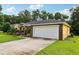 Exterior view of home showcasing a two-car garage, a driveway, and lush landscaping at 395 Alcazar Ave, De Leon Springs, FL 32130