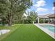 Spacious backyard with artificial turf, pool, and mature trees creating a private and serene setting at 1265 Estancia Woods Loop, Windermere, FL 34786