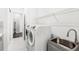 Bright laundry room with modern washer and dryer, utility sink, and storage shelving at 6348 Mossy Oak Rd, St Cloud, FL 34771