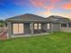 Covered patio with dining table and grill overlooking the lawn in this home's backyard at dusk at 1540 Orange Valley Rdg, Ocoee, FL 34761