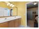 Bathroom with double sink vanity, decorative mirror, yellow walls, and an open doorway to the bedroom at 13626 Sunset Lakes Cir, Winter Garden, FL 34787