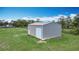 Gray outbuilding featuring a roll-up door, a side door, and metal siding, set on a green lawn at 4160 Packard Avenue, St Cloud, FL 34772